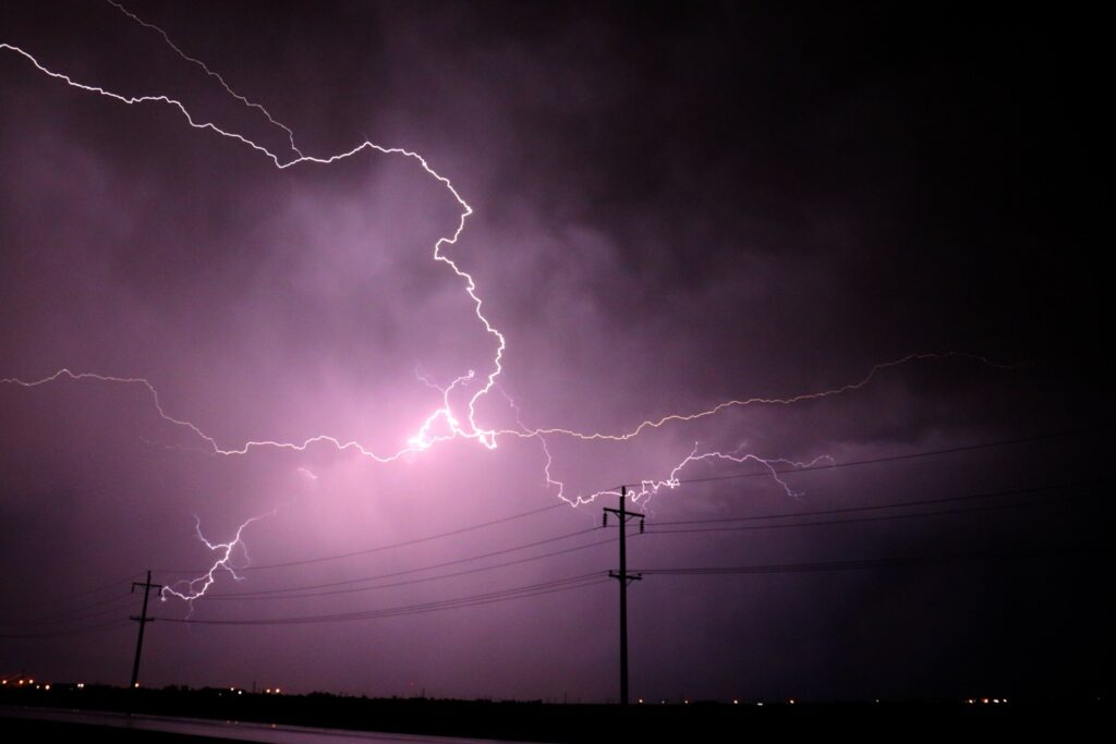 Lightning strikes across a night sky above power lines during a severe thunderstorm.